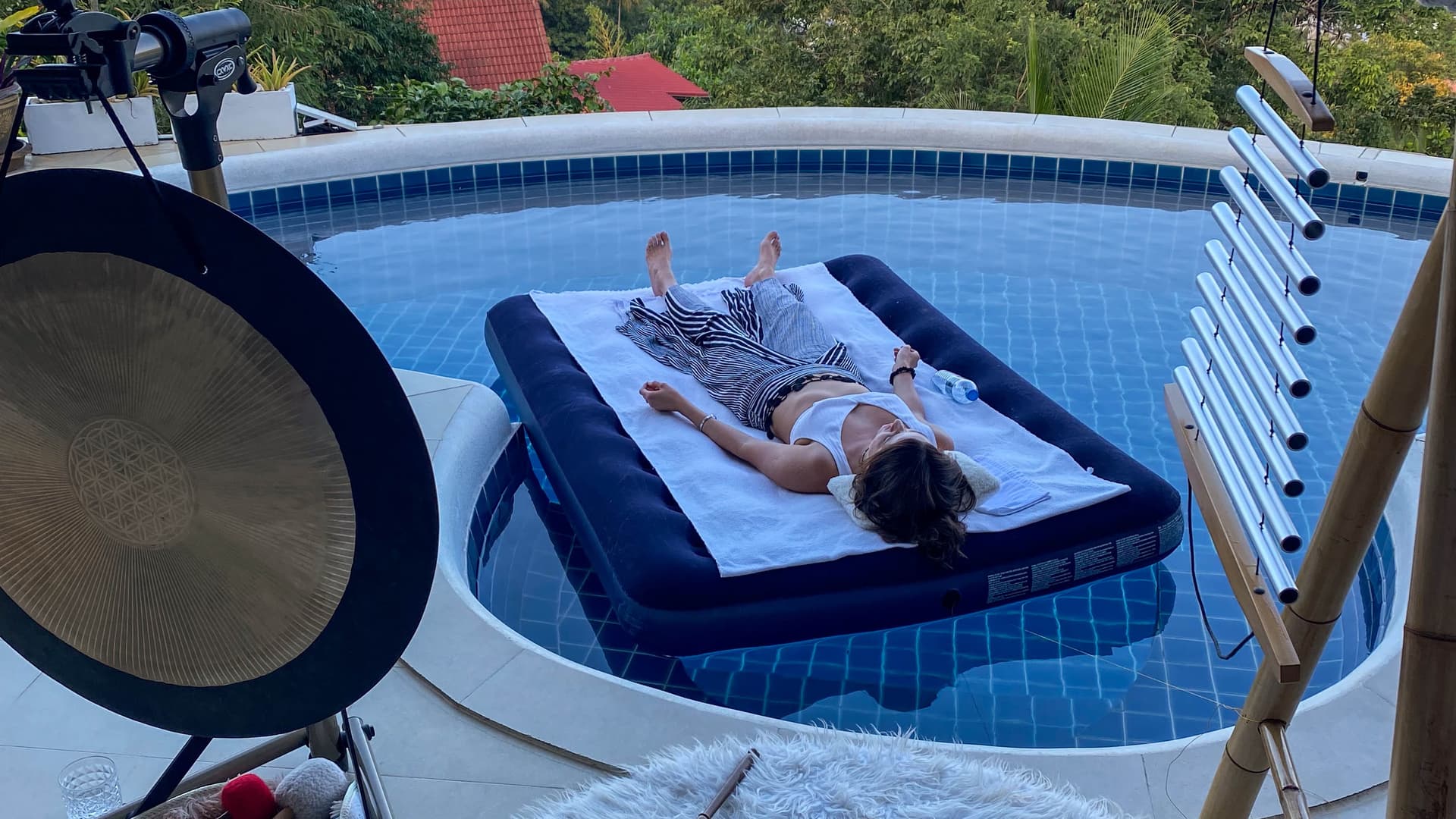 Floating sound bath session with a guest relaxing on a pool airmat at sunset.